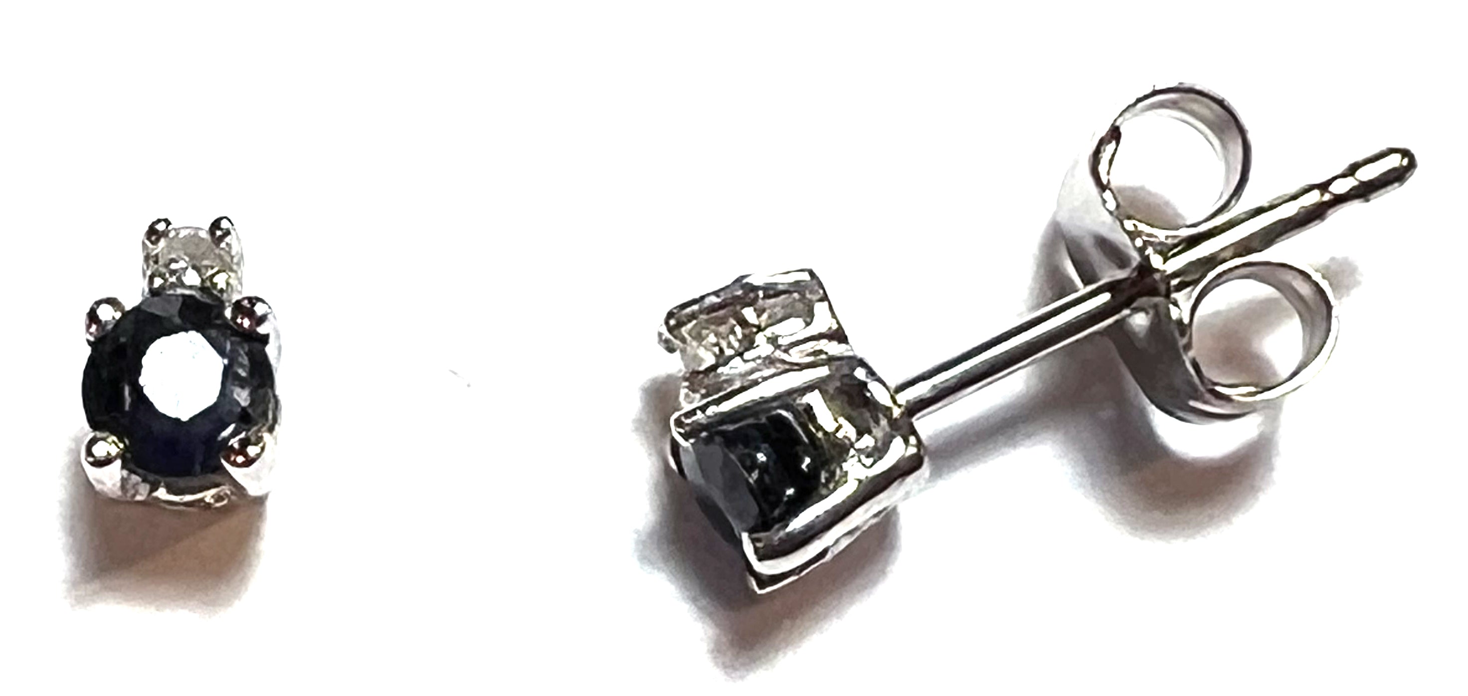 Close-up of 14kt white gold stud earrings featuring deep blue sapphires with single cut diamond accents, elegant luxury jewelry.