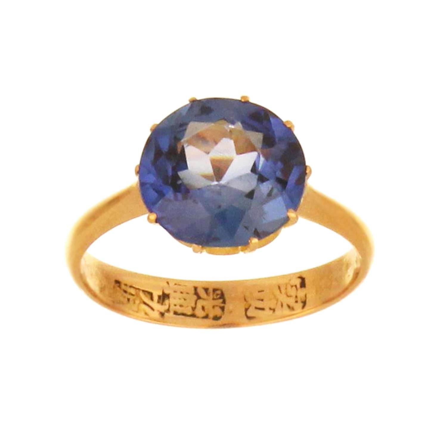 Close-up of 10 claw setting securing round synthetic blue sapphire on 21kt yellow gold ring