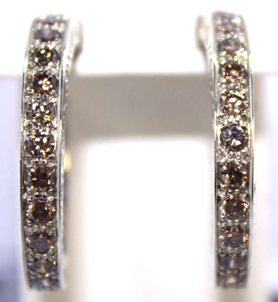 Close-up of 18kt white gold diamond hoop earrings showcasing round brilliant cut diamonds, fancy brownish-orange and white diamonds, elegant curve