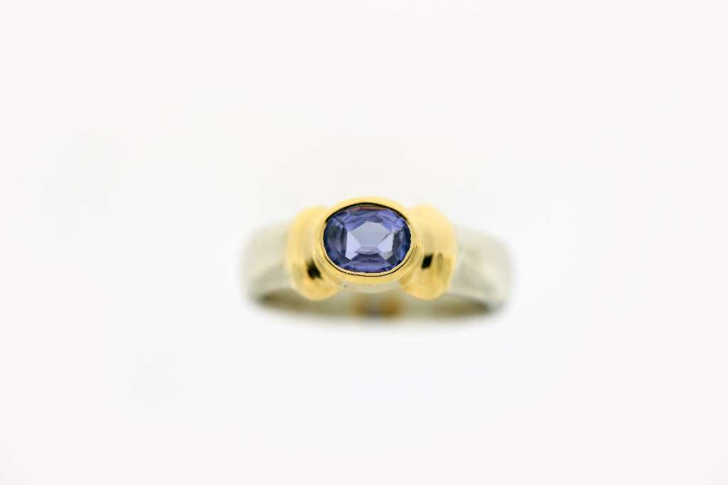 Close-up side view of 18K yellow and white gold ring showcasing bezel-set oval purple tanzanite