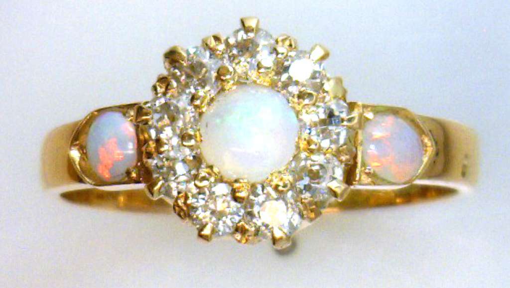 Close-up of 18kt yellow gold ring featuring three white opals and nine bezel-set old cut diamonds, displaying vintage craftsmanship and intricate detail