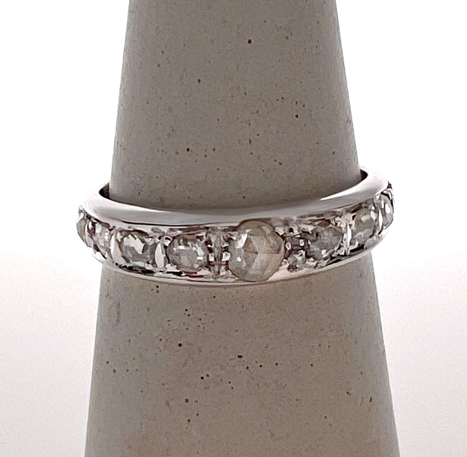 Close-up of antique 18kt white gold diamond band ring featuring nine old rose cut diamonds in bead setting on finger