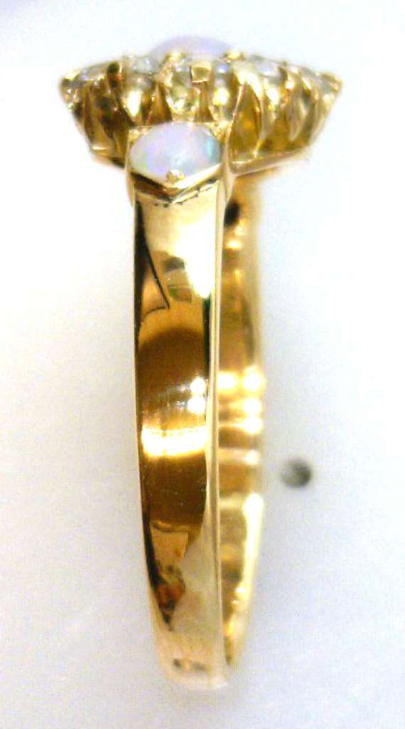 Side view of 18kt yellow gold opal and diamond ring showcasing bezel settings and smooth band with luminous white opals