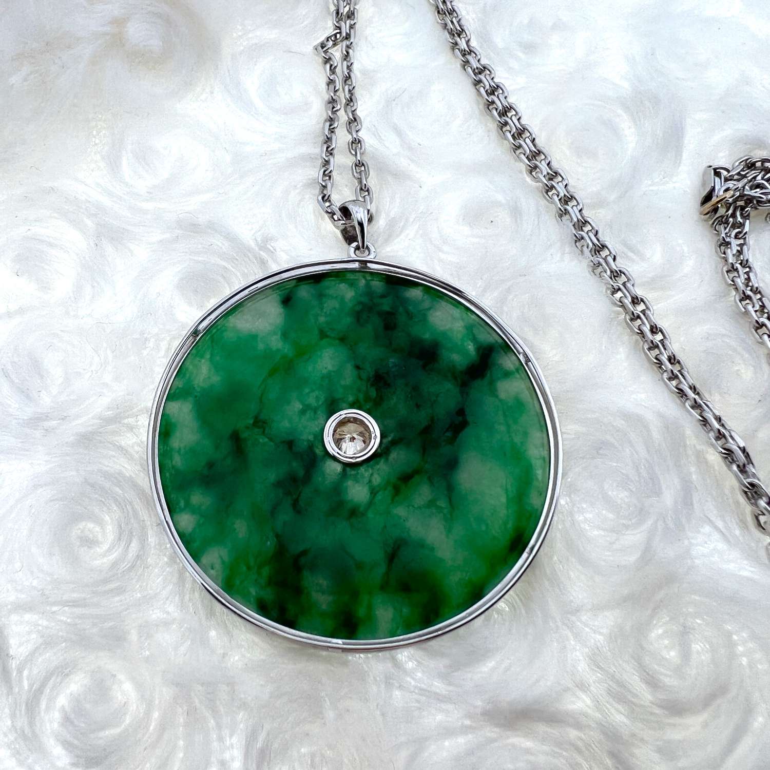 18kt white gold pendant featuring a translucent green jadeite jade donut disc with dark inclusions, viewed from front close-up showing bezel-set central diamond