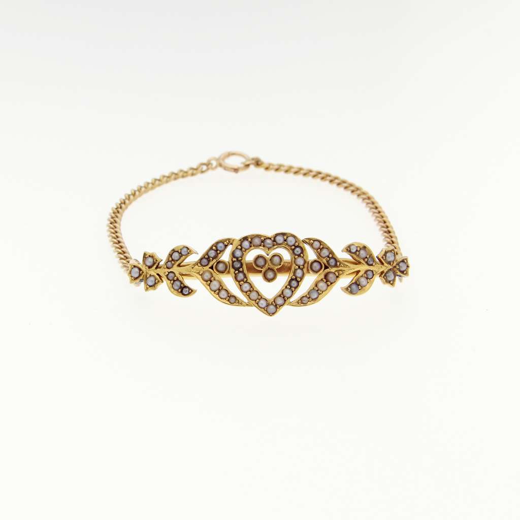 Close-up angle of 14kt yellow gold bracelet with heart-shaped motif featuring 55 white seed pearls connected by curb link chain