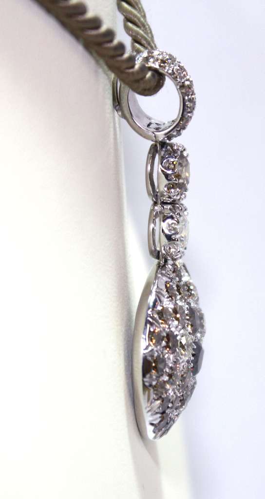 Close-up angle of 18kt white gold pendant highlighting round brilliant cut diamonds and ruby accents