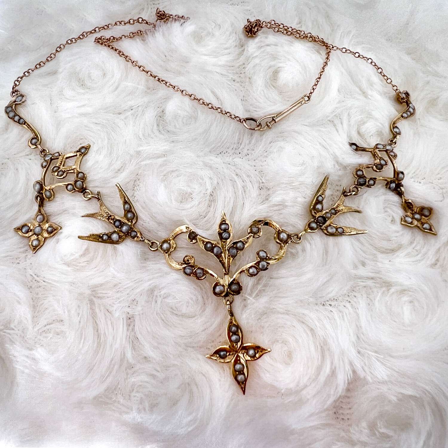 Close-up of 14kt yellow gold necklace with white round seed pearls in floral and bird motif on cable chain