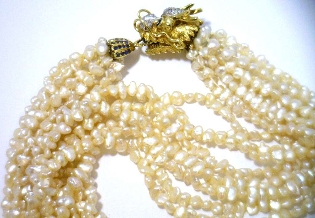 Close-up of 14kt yellow gold dragon clasp adorned with 2 round blue sapphires and 17 single cut diamonds on freshwater pearl necklace