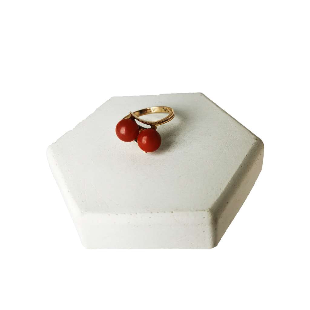 Close-up of 10kt rose gold ring featuring two vibrant red coral beads, showing side profile and band details