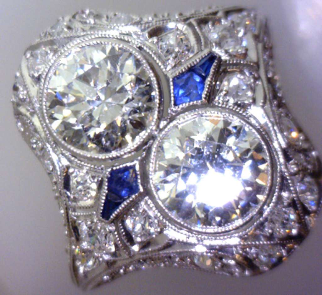Angled view highlighting the intricate bezel settings of round brilliant diamonds and four blue sapphire stones on a platinum 5.32-gram ring